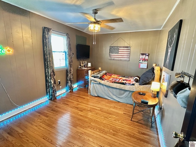 bedroom featuring crown molding, ceiling fan, wooden walls, and light hardwood / wood-style floors