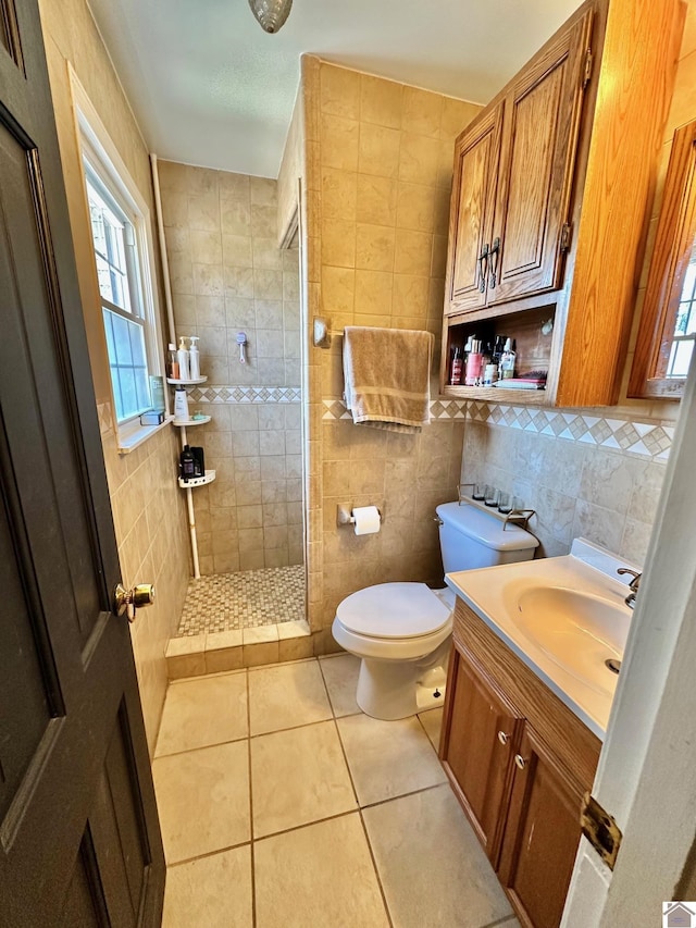 bathroom with tile patterned flooring, tile walls, a tile shower, vanity, and toilet