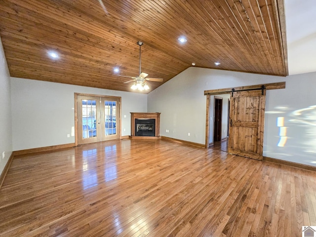 unfurnished living room with wood ceiling, vaulted ceiling, ceiling fan, a barn door, and hardwood / wood-style floors