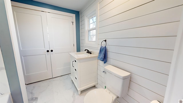 bathroom with vanity, toilet, and wood walls