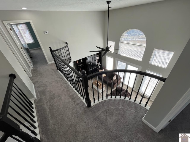 stairway with a towering ceiling, a textured ceiling, ceiling fan, and carpet flooring