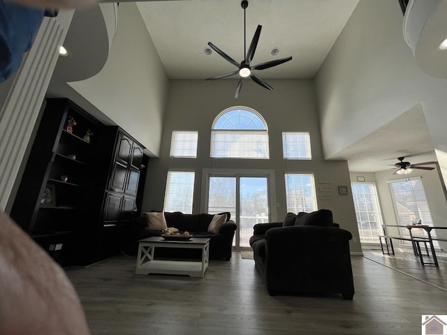 living room featuring ceiling fan, wood-type flooring, and a towering ceiling