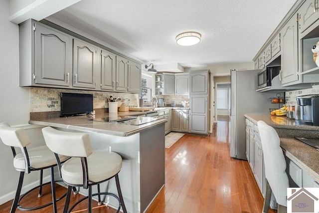 kitchen with decorative backsplash, gray cabinets, kitchen peninsula, and a kitchen bar