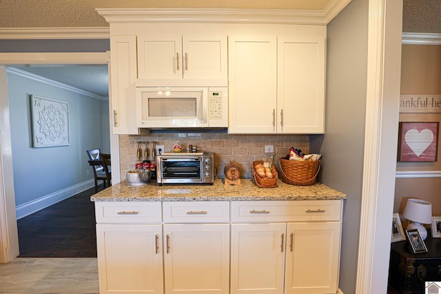 kitchen with white cabinetry, light stone counters, decorative backsplash, and crown molding