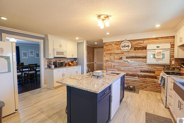 kitchen featuring sink, white appliances, white cabinetry, light stone counters, and an island with sink