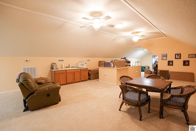 dining room featuring visible vents, ceiling fan, vaulted ceiling, light carpet, and a textured ceiling