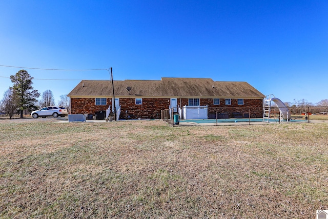 rear view of property featuring fence, a lawn, and an outdoor pool