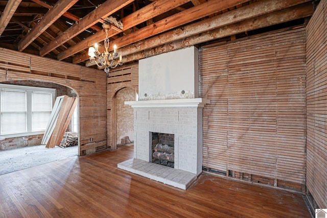 unfurnished living room with a notable chandelier, hardwood / wood-style flooring, a fireplace, and beamed ceiling