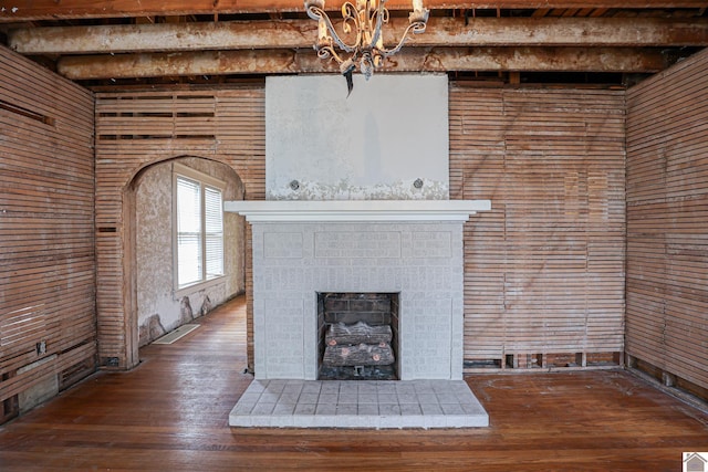 unfurnished living room with hardwood / wood-style floors, beam ceiling, a brick fireplace, and wood walls