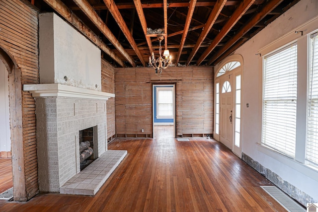 unfurnished living room with an inviting chandelier, hardwood / wood-style floors, a fireplace, and a healthy amount of sunlight