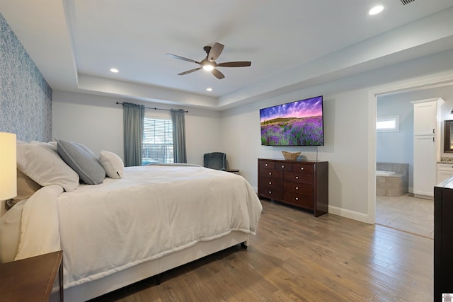 bedroom with ensuite bathroom, light wood-type flooring, ceiling fan, and a tray ceiling