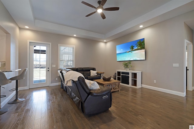 living room with dark hardwood / wood-style floors, a raised ceiling, and ceiling fan