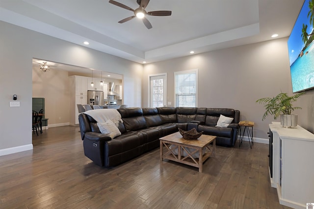 living room featuring dark wood-type flooring, ceiling fan, and a tray ceiling