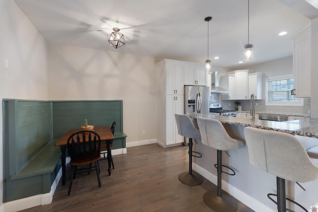 kitchen with appliances with stainless steel finishes, white cabinets, hanging light fixtures, light stone countertops, and wall chimney exhaust hood