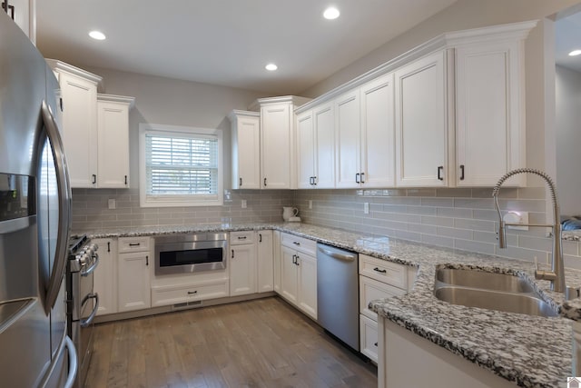 kitchen with sink, appliances with stainless steel finishes, light stone counters, white cabinets, and decorative backsplash