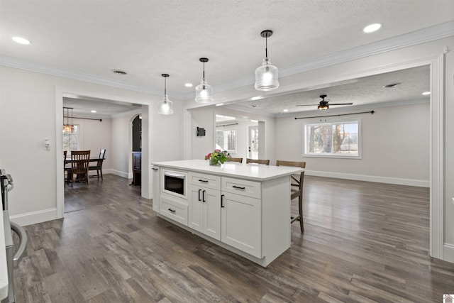 kitchen with built in microwave, a kitchen island, pendant lighting, and white cabinets