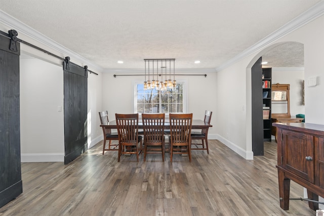 dining space with hardwood / wood-style flooring, ornamental molding, and a barn door