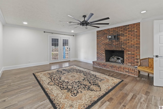 living room featuring a brick fireplace, a textured ceiling, ornamental molding, ceiling fan, and hardwood / wood-style floors