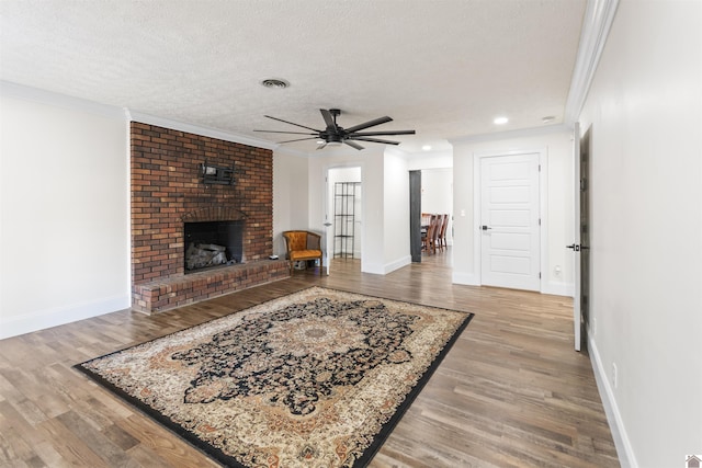 living room featuring light hardwood / wood-style flooring, ceiling fan, ornamental molding, a textured ceiling, and a brick fireplace