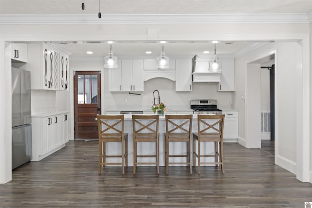 kitchen with premium range hood, decorative light fixtures, appliances with stainless steel finishes, an island with sink, and white cabinets