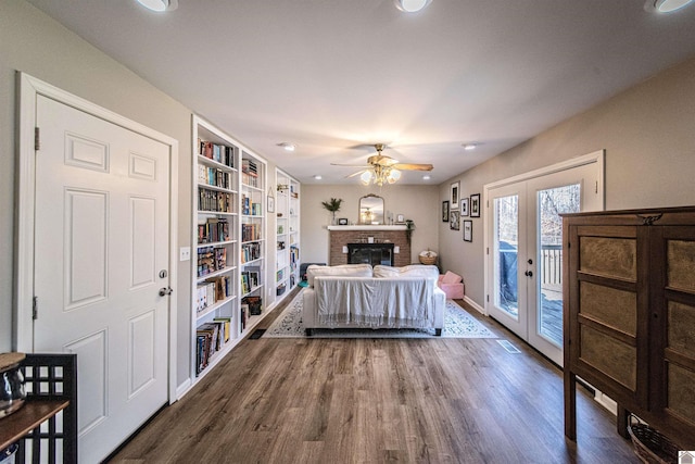 bedroom with dark wood-type flooring, ceiling fan, access to exterior, a fireplace, and french doors