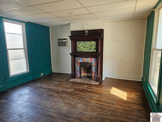 unfurnished living room with an AC wall unit, a paneled ceiling, a fireplace, dark hardwood / wood-style flooring, and plenty of natural light