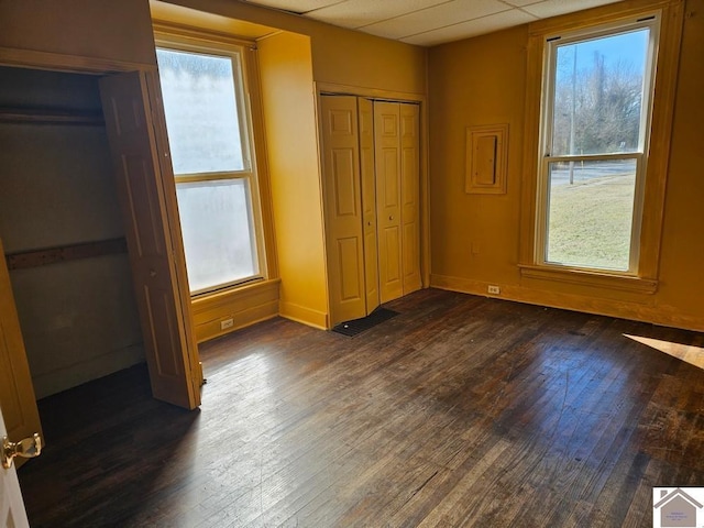 unfurnished bedroom featuring a paneled ceiling, dark hardwood / wood-style flooring, and multiple windows