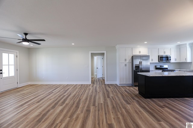 kitchen with hardwood / wood-style flooring, ceiling fan, stainless steel appliances, light stone countertops, and white cabinets