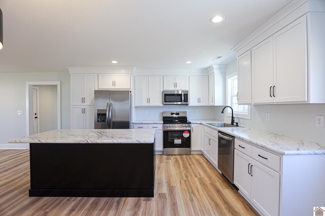 kitchen with appliances with stainless steel finishes, white cabinetry, sink, a center island, and light stone counters