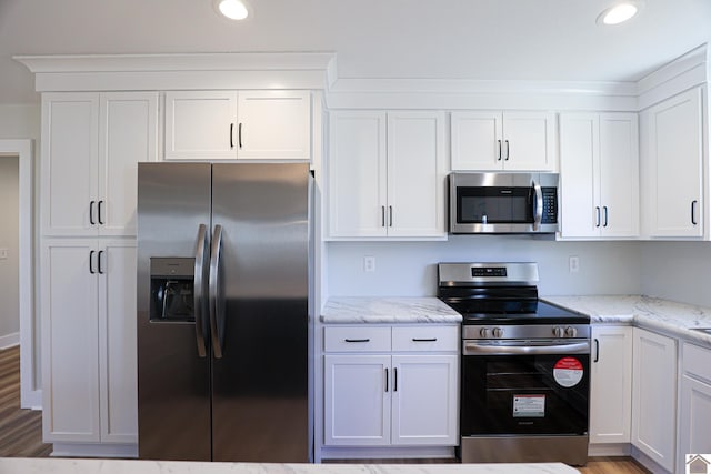 kitchen with light stone countertops, appliances with stainless steel finishes, white cabinets, and light wood-type flooring