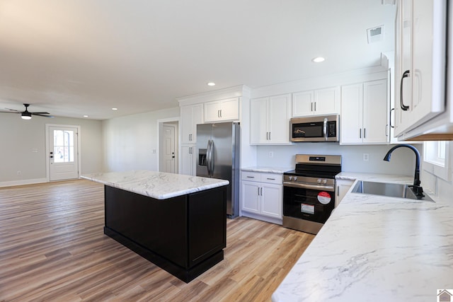 kitchen featuring sink, white cabinetry, light stone counters, a center island, and stainless steel appliances