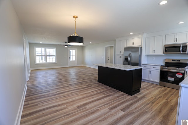 kitchen featuring appliances with stainless steel finishes, white cabinetry, light stone countertops, light hardwood / wood-style floors, and a kitchen island