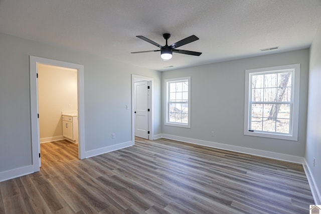 unfurnished bedroom featuring multiple windows, dark wood-type flooring, connected bathroom, and ceiling fan