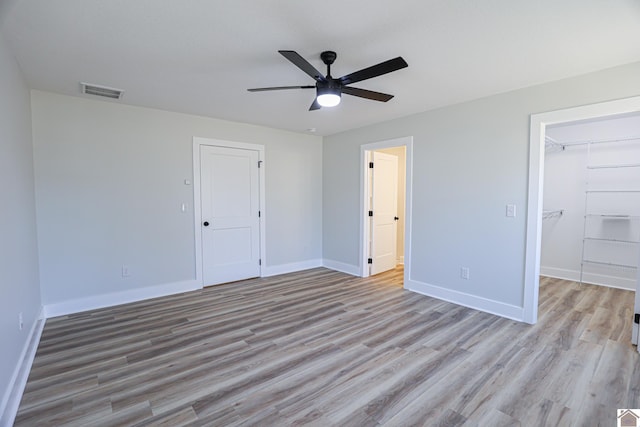 unfurnished bedroom with a closet, a spacious closet, ceiling fan, and light hardwood / wood-style flooring