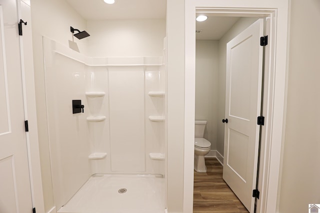 bathroom with hardwood / wood-style floors, a shower, and toilet