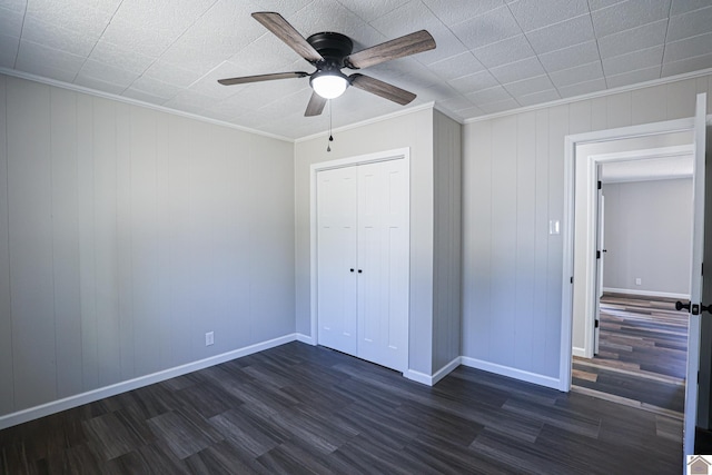 unfurnished bedroom with dark wood-type flooring, ornamental molding, a closet, and ceiling fan