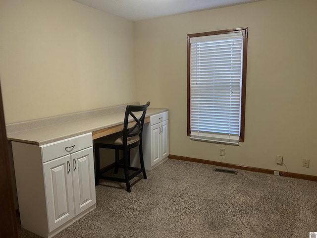 unfurnished office featuring built in desk and light colored carpet