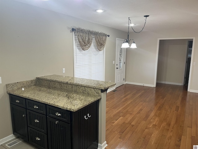 kitchen featuring pendant lighting, dark hardwood / wood-style floors, an inviting chandelier, and light stone counters