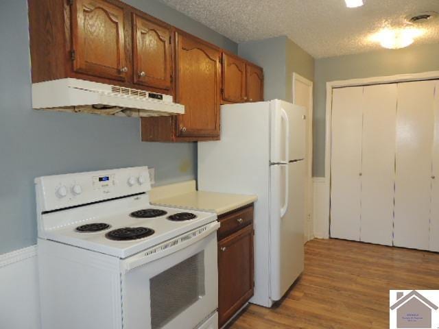 kitchen with light wood-type flooring, a textured ceiling, and white appliances