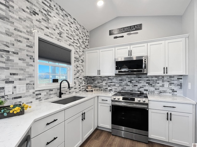 kitchen with vaulted ceiling, white cabinetry, sink, stainless steel appliances, and light stone countertops