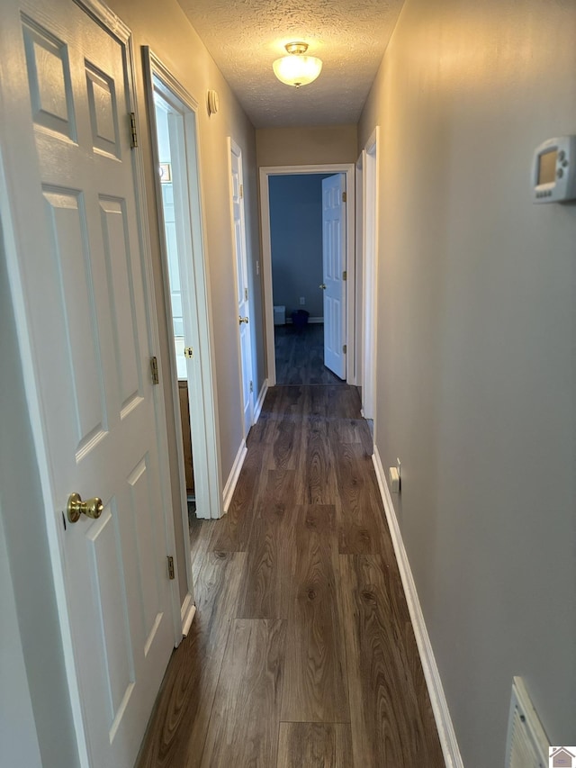 corridor with dark hardwood / wood-style floors and a textured ceiling