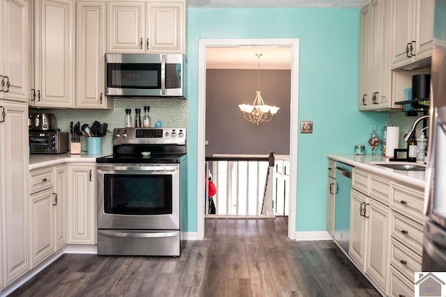 kitchen featuring dark wood-style flooring, stainless steel appliances, light countertops, a sink, and a chandelier