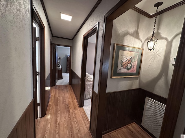 corridor with light hardwood / wood-style flooring, ornamental molding, and wooden walls