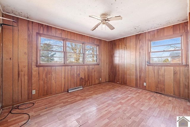 spare room with ceiling fan, light hardwood / wood-style flooring, and wood walls