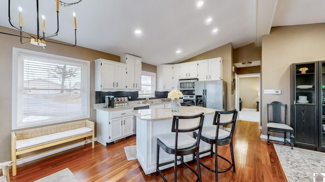 kitchen with lofted ceiling, hanging light fixtures, appliances with stainless steel finishes, a kitchen island, and white cabinets