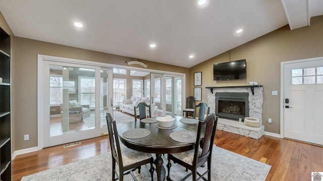 dining space with lofted ceiling, hardwood / wood-style flooring, a stone fireplace, and french doors