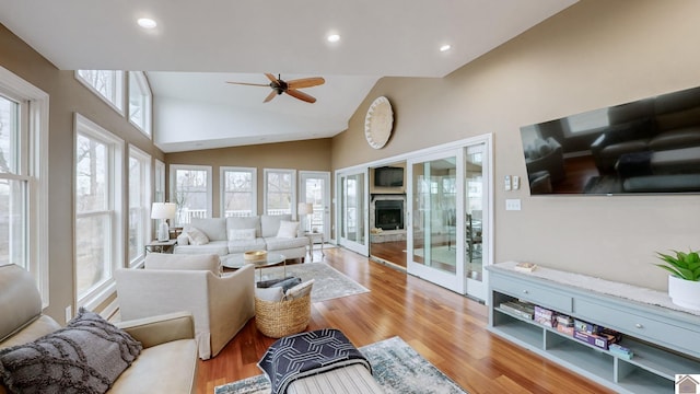 living room featuring ceiling fan, high vaulted ceiling, a fireplace, and light hardwood / wood-style flooring