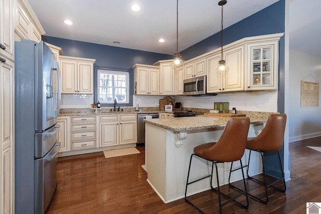 kitchen featuring sink, a breakfast bar, appliances with stainless steel finishes, hanging light fixtures, and light stone countertops