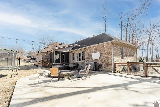 rear view of property with a trampoline, a patio area, and an outdoor fire pit