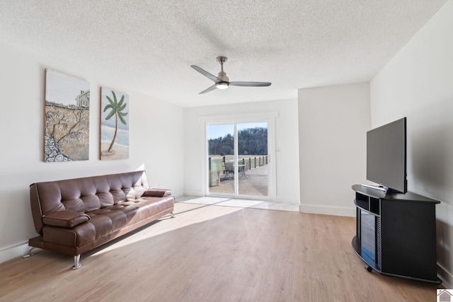 living area with ceiling fan, a textured ceiling, and light wood-type flooring